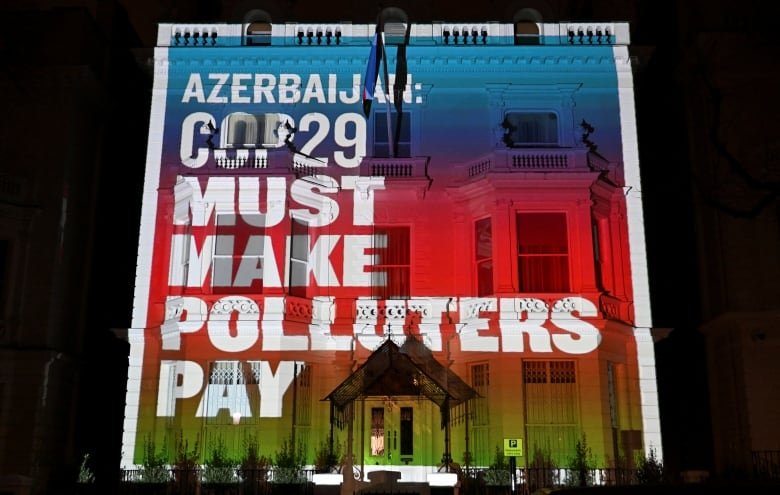 A building is covered in a colourful projection that says in white letters: "Azerbaijan COP29 MUST MAKE POLLUTERS PAY".