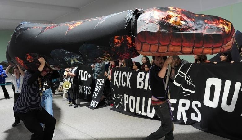 Activists carry a giant model of a red and black snake above their heads, walking in front of another big group of people holding a banner that says "Kick big polluters out" with the image of a boot.