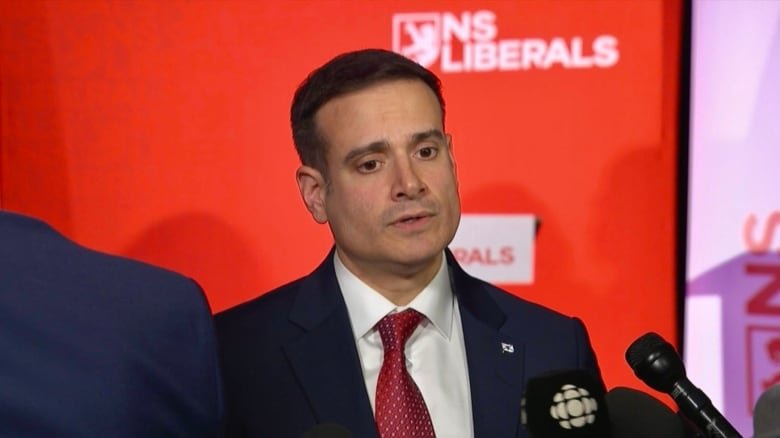 A man wearing a suit looks down to the ground as microphones are pointed toward his face.