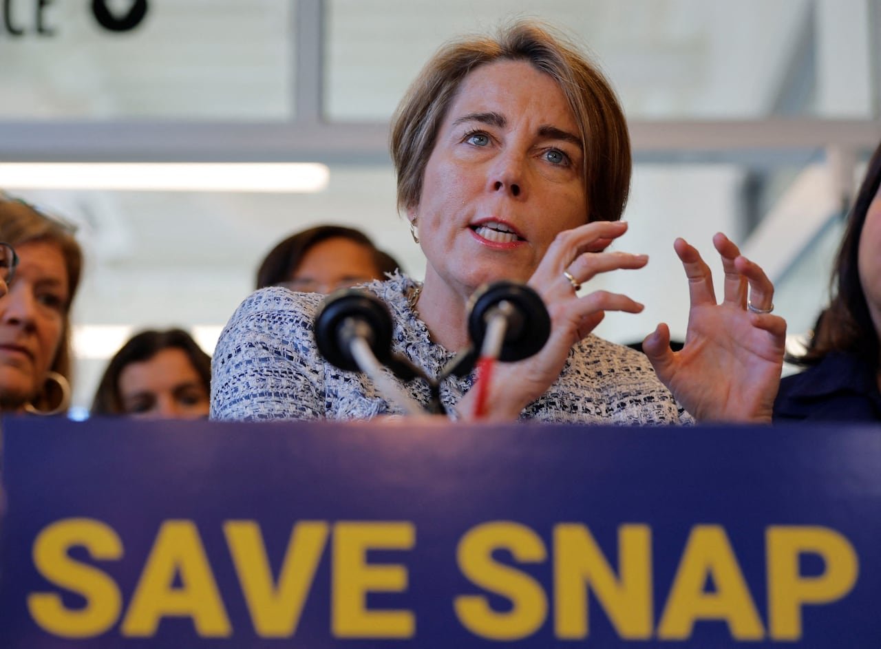 A woman with ear-length hair gestures while speaking at a podium with a sign reading, "Save Snap."