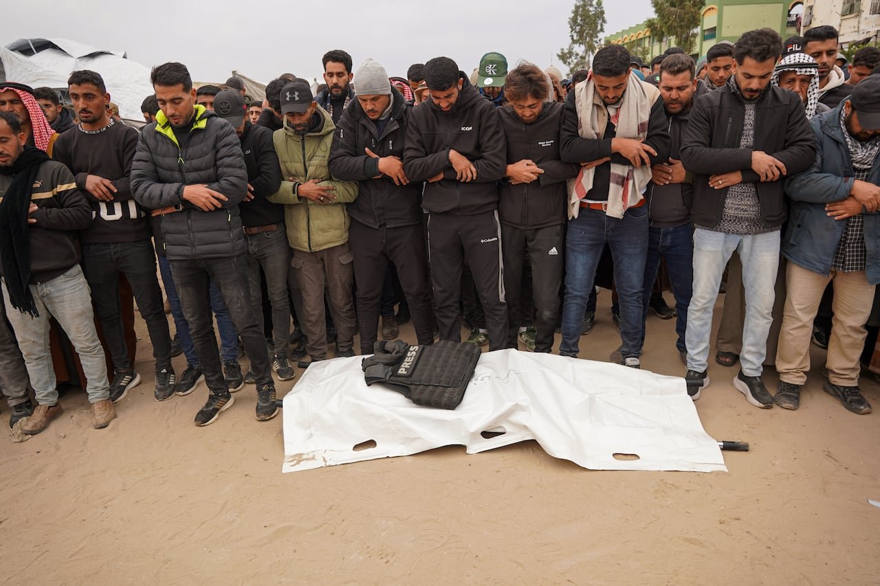 A group of individuals standing solemnly by a shrouded deceased body with a 