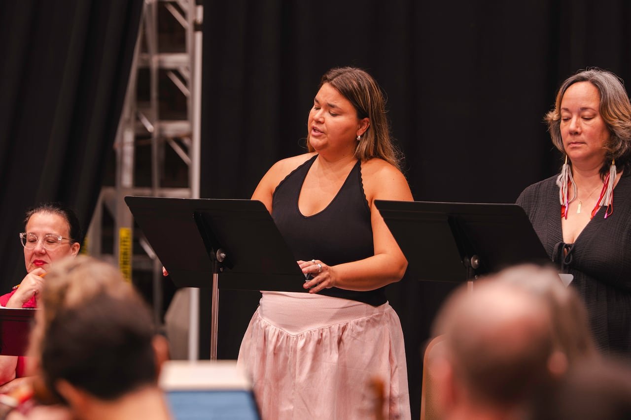 A woman in a pink dress and black halter top singing with a music stand in front of her, accompanied by another woman standing beside her behind a music stand.