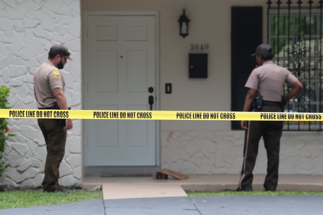Police officers outside a door with caution tape reading: Police Line do not cross