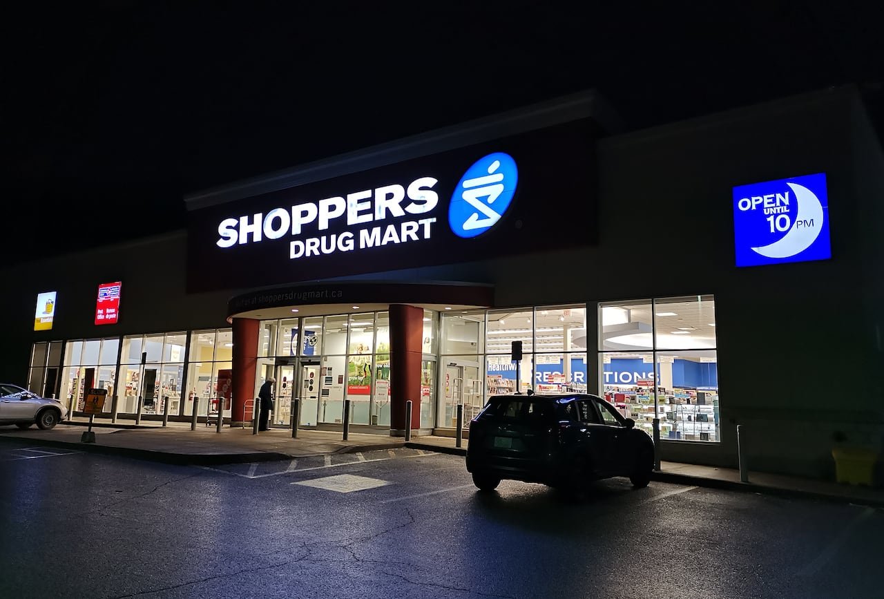 a shoppers drug mart sign on a storefront glows against a dark night sky